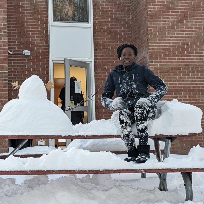 A student sitting outside in deep snow beside a campus building